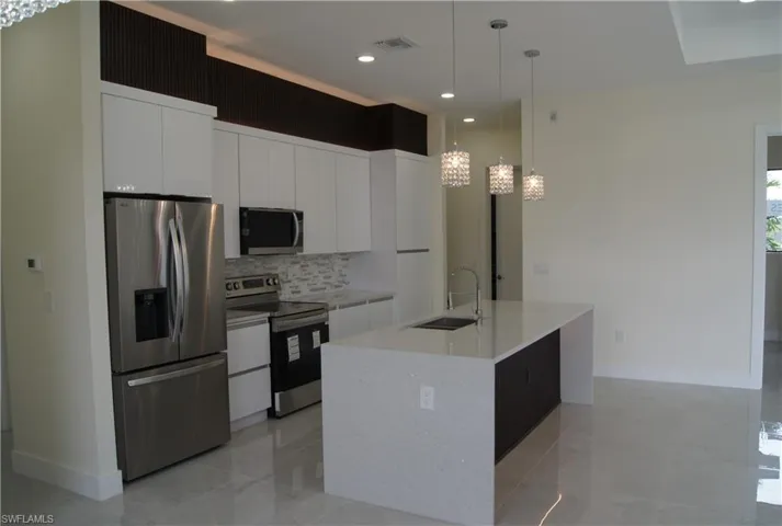 Kitchen featuring white cabinets, appliances with stainless steel finishes, decorative light fixtures, a kitchen island with sink, and a sink