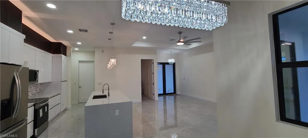 Kitchen featuring appliances with stainless steel finishes, pendant lighting, a raised ceiling, sink, and white cabinetry