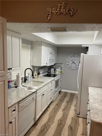 Kitchen featuring white appliances, backsplash, white cabinets, light wood-style flooring, and a tray ceiling