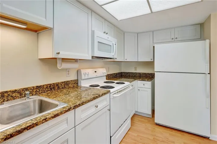 Kitchen with white cabinetry, sink, light hardwood / wood-style flooring, dark stone counters, and white appliances