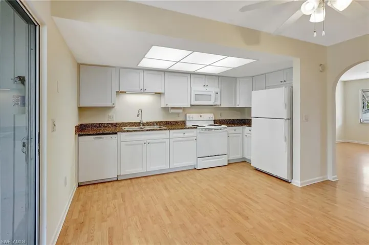 Kitchen featuring white appliances, white cabinets, sink, light hardwood / wood-style flooring, and ceiling fan