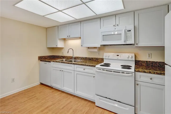 Kitchen with white appliances, dark stone counters, sink, light wood-type flooring, and white cabinetry