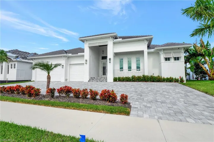 Modern white stucco exterior featuring a grand entrance, paver driveway, two-car garage, and established landscaping
