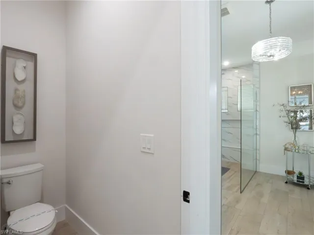 Modern bathroom featuring a frameless glass shower enclosure with wood-finish flooring, white subway tile surround, contemporary pendant lighting, and a separate water closet with ceramic fixtures