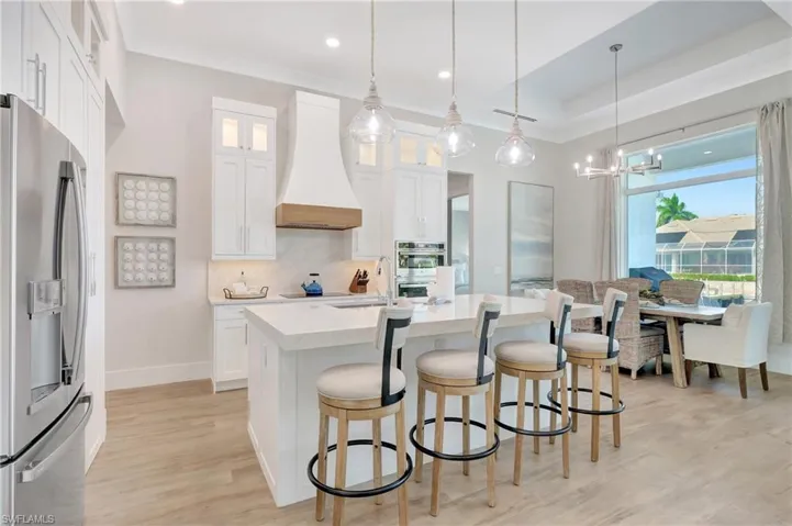 Gourmet kitchen featuring a substantial island with seating, pendant lighting, white cabinetry, a built-in stainless steel refrigerator, and wood-finish flooring