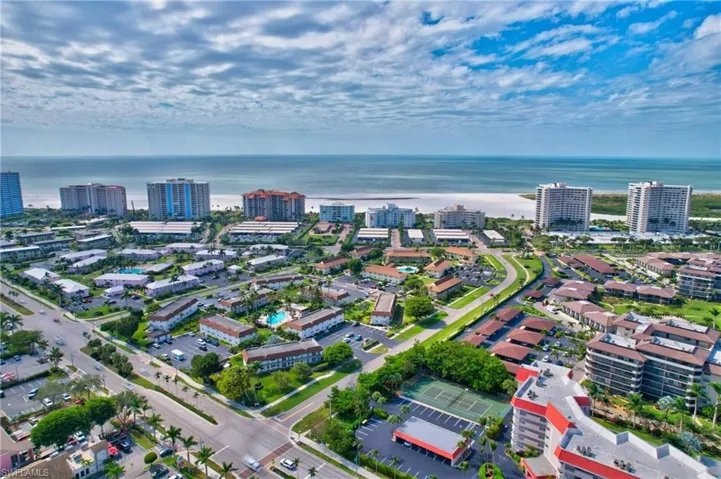 Coastal community featuring diverse residential structures, extensive paved roads, a tennis court, multiple swimming pools, and broad beachfront access