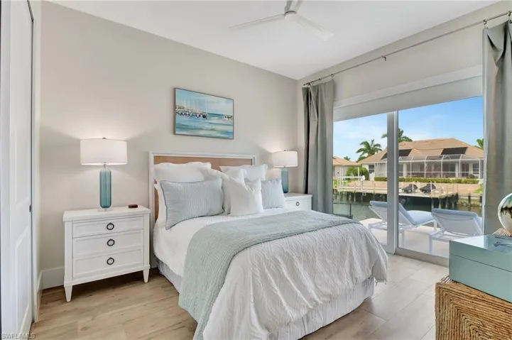 Bedroom featuring wood-finish flooring, a ceiling fan, and sliding glass doors opening to a waterfront patio