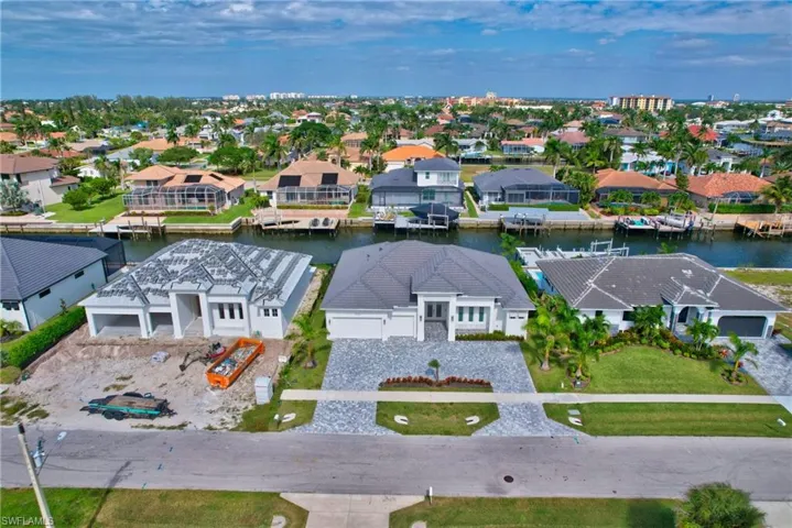 Waterfront property with direct canal access, featuring a paved driveway, a manicured lawn, and a modern exterior with a dark tile roof