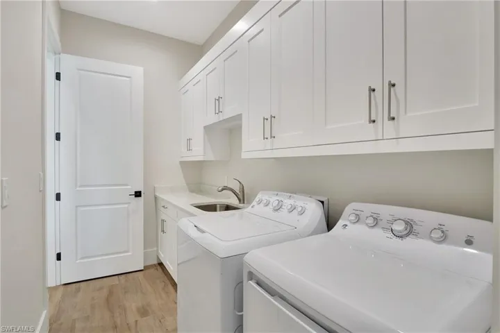 Laundry room featuring white shaker cabinetry, stainless steel sink, light-toned countertop, wood-finish flooring, and a white interior door with black hardware