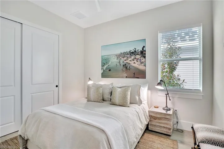 Light-filled room featuring a double-pane window with blinds, white walls, and wood-finish flooring