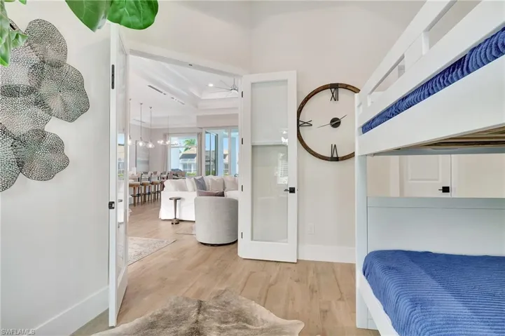 White double doors with frosted glass panels open to reveal an expansive open-concept living space with wood-finish flooring, a coffered ceiling, and pendant lighting