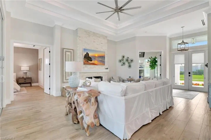 Spacious living area featuring light wood-finish flooring and a multi-tiered tray ceiling with a contemporary ceiling fan