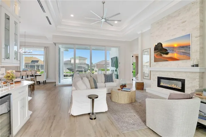 Spacious living area featuring expansive glass sliding doors, wood-finish flooring, a contemporary fireplace with a stone surround, and a coffered ceiling