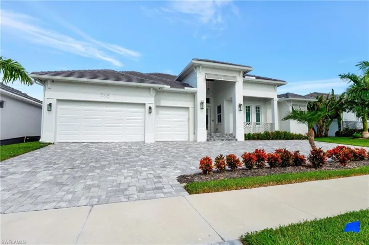 Contemporary white stucco exterior with a covered entry, paver driveway, two-car garage, and established landscaping
