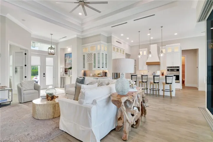 Open-concept living space featuring high tray ceilings, wood-finish flooring, and a contemporary kitchen with a large island