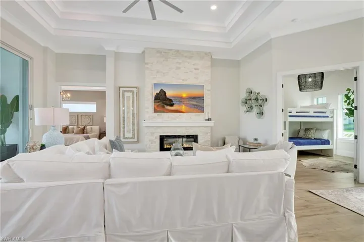 Living area featuring a stone-clad fireplace with an integrated linear electric insert, a tray ceiling, wood-finish flooring, and recessed lighting