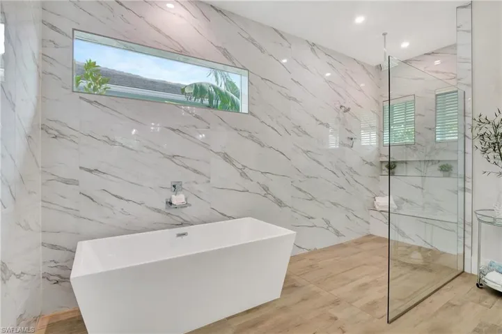 Contemporary bathroom featuring large format marble-look wall tiles, a freestanding soaking tub with wall-mounted fixtures, and a glass-enclosed shower with multiple recessed shelves
