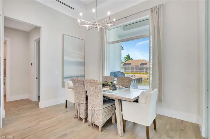 Dining area featuring wood-finish flooring, a contemporary chandelier, recessed ceiling, and a large window overlooking a waterway