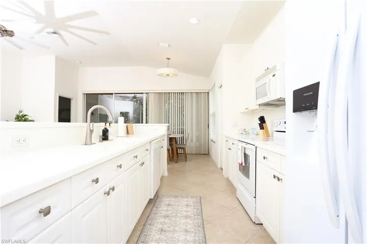 Kitchen featuring white appliances, vaulted ceiling, ceiling fan, white cabinets, and light tile patterned flooring