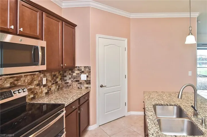 Kitchen featuring stainless steel appliances, light stone counters, backsplash, pendant lighting, and sink