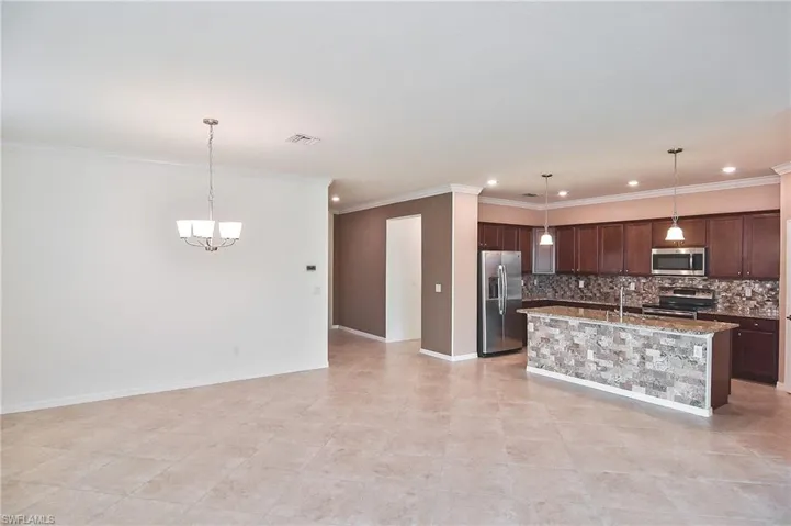 Kitchen featuring decorative light fixtures, light tile flooring, backsplash, a center island with sink, and appliances with stainless steel finishes