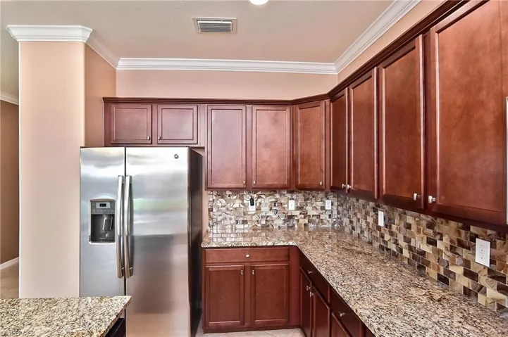 Kitchen with ornamental molding, tasteful backsplash, stainless steel fridge, and light stone countertops
