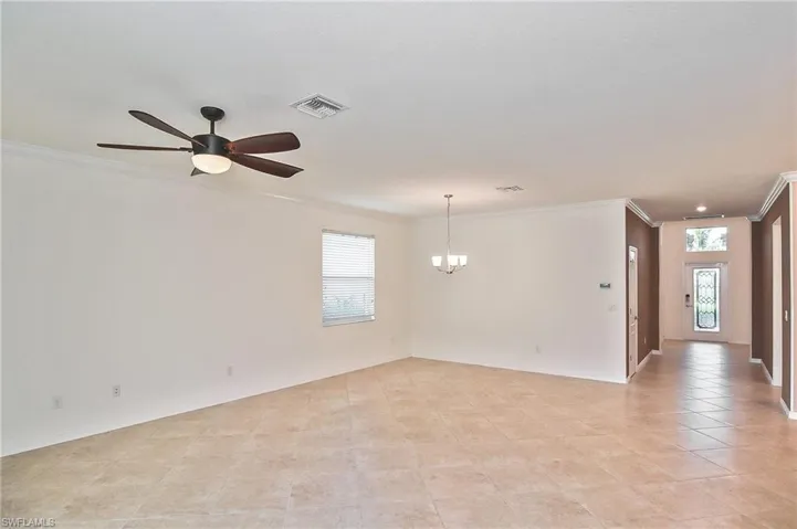 Spare room with crown molding, light tile flooring, and ceiling fan with notable chandelier