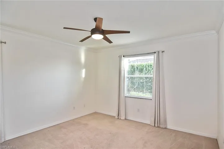 Carpeted spare room with crown molding and ceiling fan