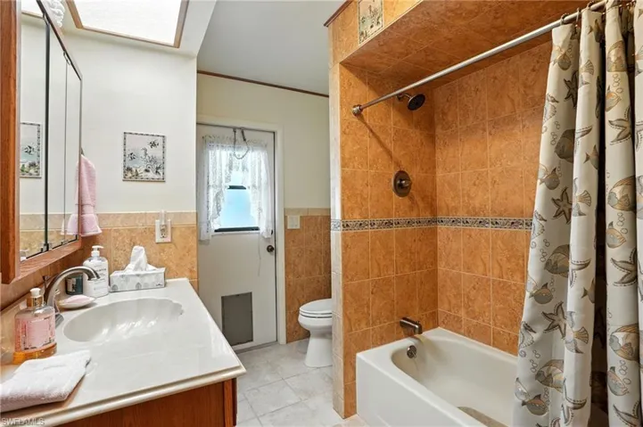 Full bath with shower / tub combo with curtain, vanity, ornamental molding, light tile patterned floors, and tile walls