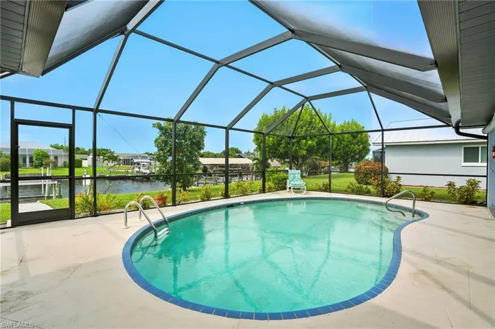 Swimming pool featuring a lanai, a sunroom, a water view, a lawn, and a patio