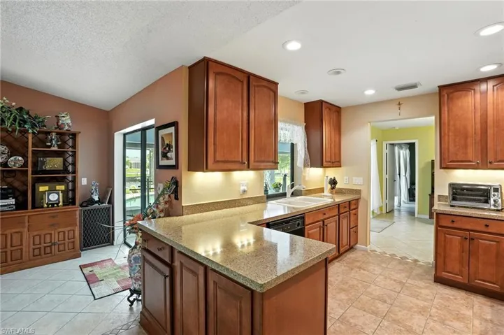 Kitchen featuring light tile patterned floors, brown cabinetry, light stone counters, a peninsula, and recessed lighting