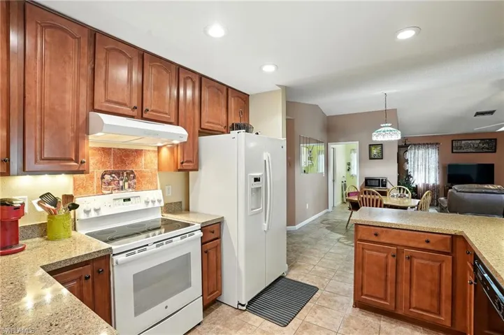 Kitchen featuring white appliances, under cabinet range hood, open floor plan, pendant lighting, and brown cabinetry