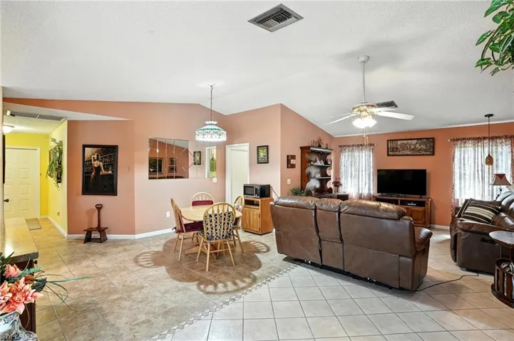 Living room with light tile patterned floors, vaulted ceiling, a textured ceiling, and ceiling fan