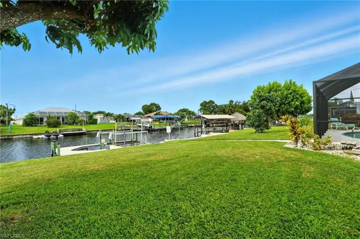 View of grassy yard featuring a water view, boat lift, a boat dock, and glass enclosure