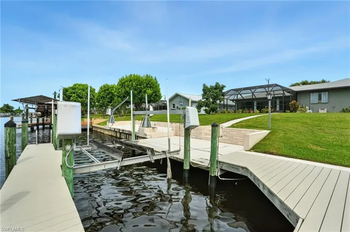 Dock area featuring boat lift, a sunroom, a water view, and a lawn