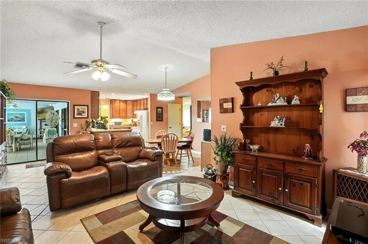Living room with a textured ceiling, light tile patterned floors, lofted ceiling, and a ceiling fan