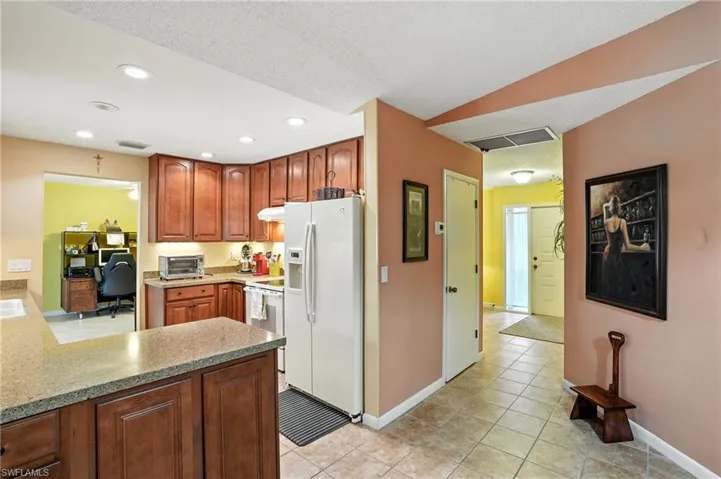 Kitchen with white appliances, light tile patterned flooring, light stone counters, a peninsula, and an office area
