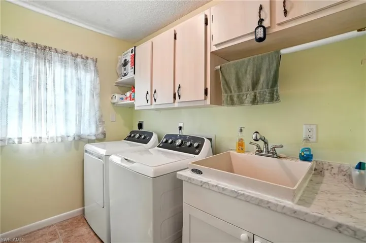 Laundry room with a textured ceiling, washing machine and dryer, cabinet space, and light tile patterned floors