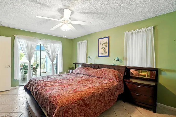 Bedroom with light tile patterned floors, access to exterior, a textured ceiling, and a ceiling fan