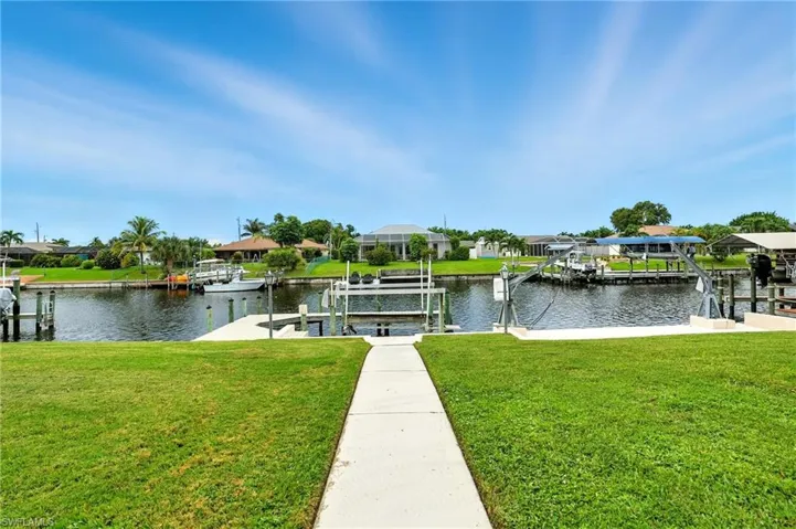 Dock area featuring boat lift, a yard, a water view, and a residential view