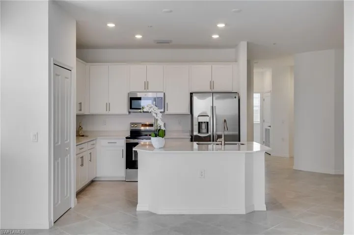 Kitchen with stainless steel appliances, white cabinetry, light stone counters, a center island with sink, and recessed lighting