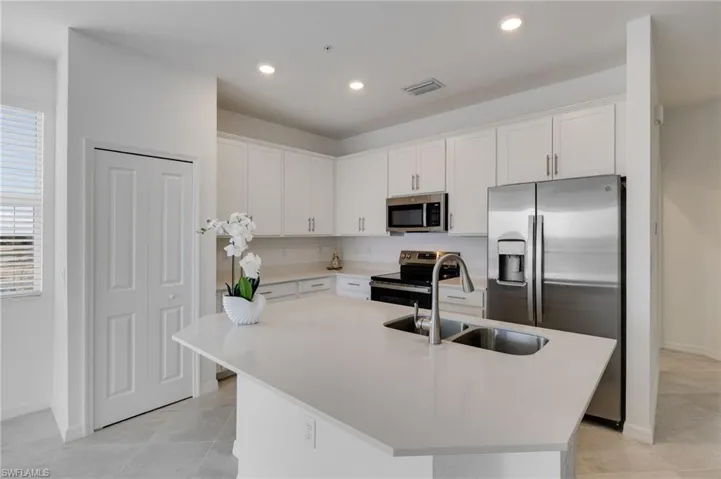 Kitchen with stainless steel appliances, white cabinets, a kitchen island with sink, light stone countertops, and recessed lighting