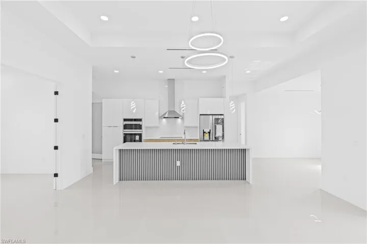 Kitchen featuring modern cabinets, white cabinets, an island with sink, stainless steel appliances, and pendant lighting