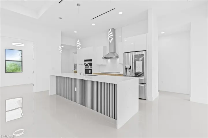 Kitchen with modern cabinets, white cabinetry, stainless steel fridge, decorative light fixtures, and an island with sink