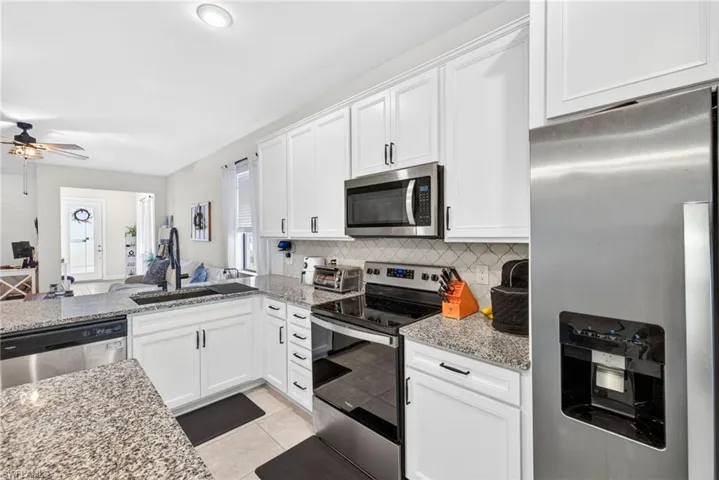Modern kitchen featuring white cabinetry, granite countertops, stainless steel appliances, and a tile backsplash