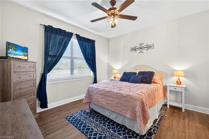 Windowed room with wood-finish flooring, a ceiling fan with light fixture, and white painted walls