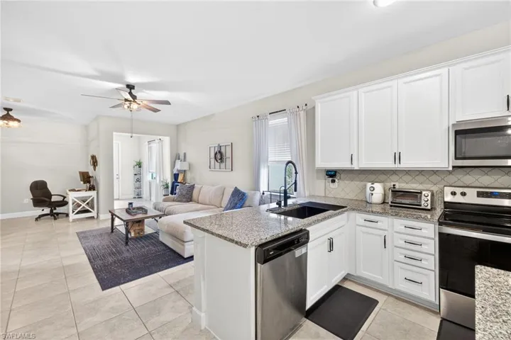 Kitchen and living area featuring granite countertops, white cabinetry, stainless steel appliances, tile flooring, and a ceiling fan