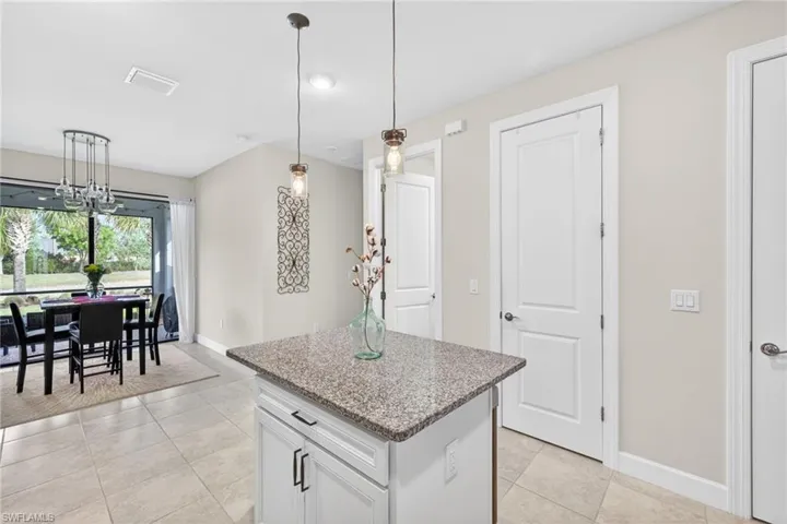 Kitchen island with a granite-style countertop, pendant lighting, and white cabinetry