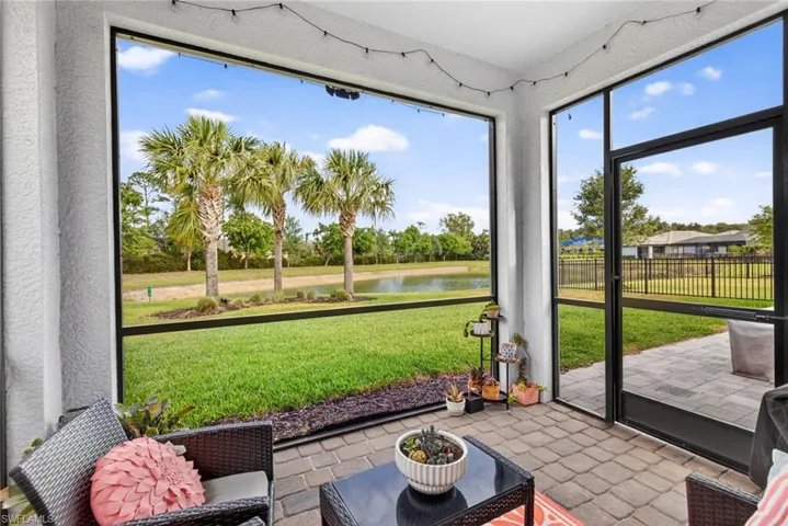 Screened lanai featuring a paver patio, a serene pond, mature palm trees, and a lush green lawn