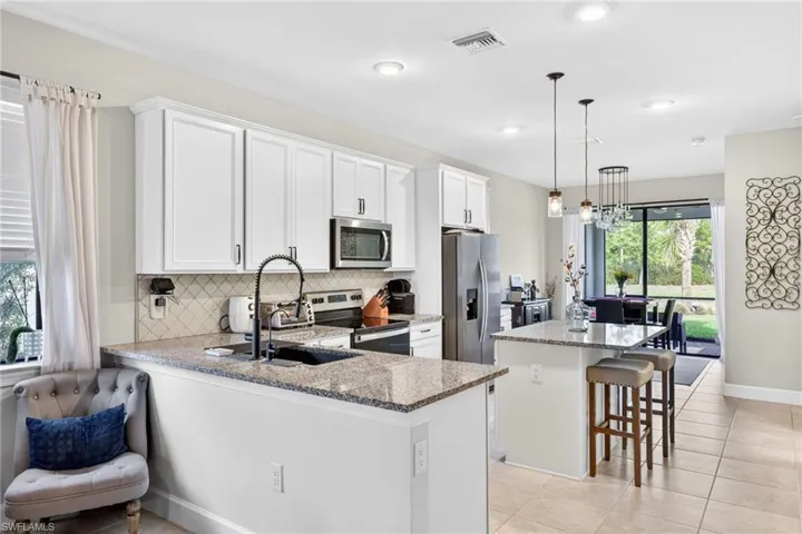 Modern kitchen featuring white cabinetry, granite countertops, a tiled backsplash, and stainless steel appliances